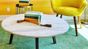 A yellow armchair, a round table with books, and a painting on the wall. - New 3 bed 4 bath home - rooftop deck, 2 car garage & porch near downtown! (Omaha)