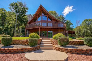 A wooden cabin with a balcony, surrounded by landscaped gardens and trees. - Bobcat Ridge~Hottub, Arcade, Clubhouse, Foosball on 11 Wooded Acres (Logan)