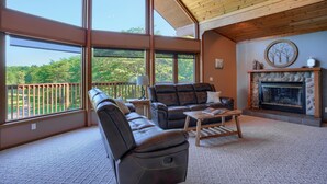 Ein geräumiges Wohnzimmer mit Kamin, Ledersofas und großen Fenstern mit Blick ins Freie.