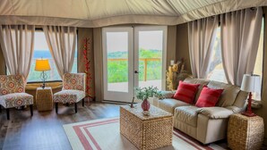 Une pièce comprenant un canapé, deux fauteuils, une table basse et offrant une vue sur la verdure par la porte.