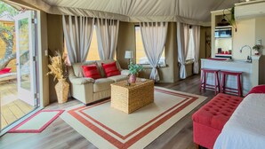 Un hébergement sous tente comprenant un canapé, un pouf et des sièges rouges, un coin cuisine et un ventilateur de plafond.