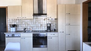 Een moderne keuken met lichte kastjes, een roestvrijstalen afzuigkap, een inbouwoven en een koffiezetapparaat.
