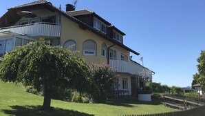 Een twee verdiepingen tellend huis met een balkon, omringd door een houten hek en een verzorgd gazon.