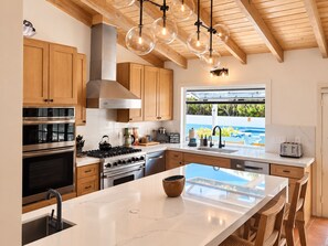Une cuisine moderne avec des meubles en bois, des appareils en acier inoxydable, un grand îlot central et une vue sur une piscine.