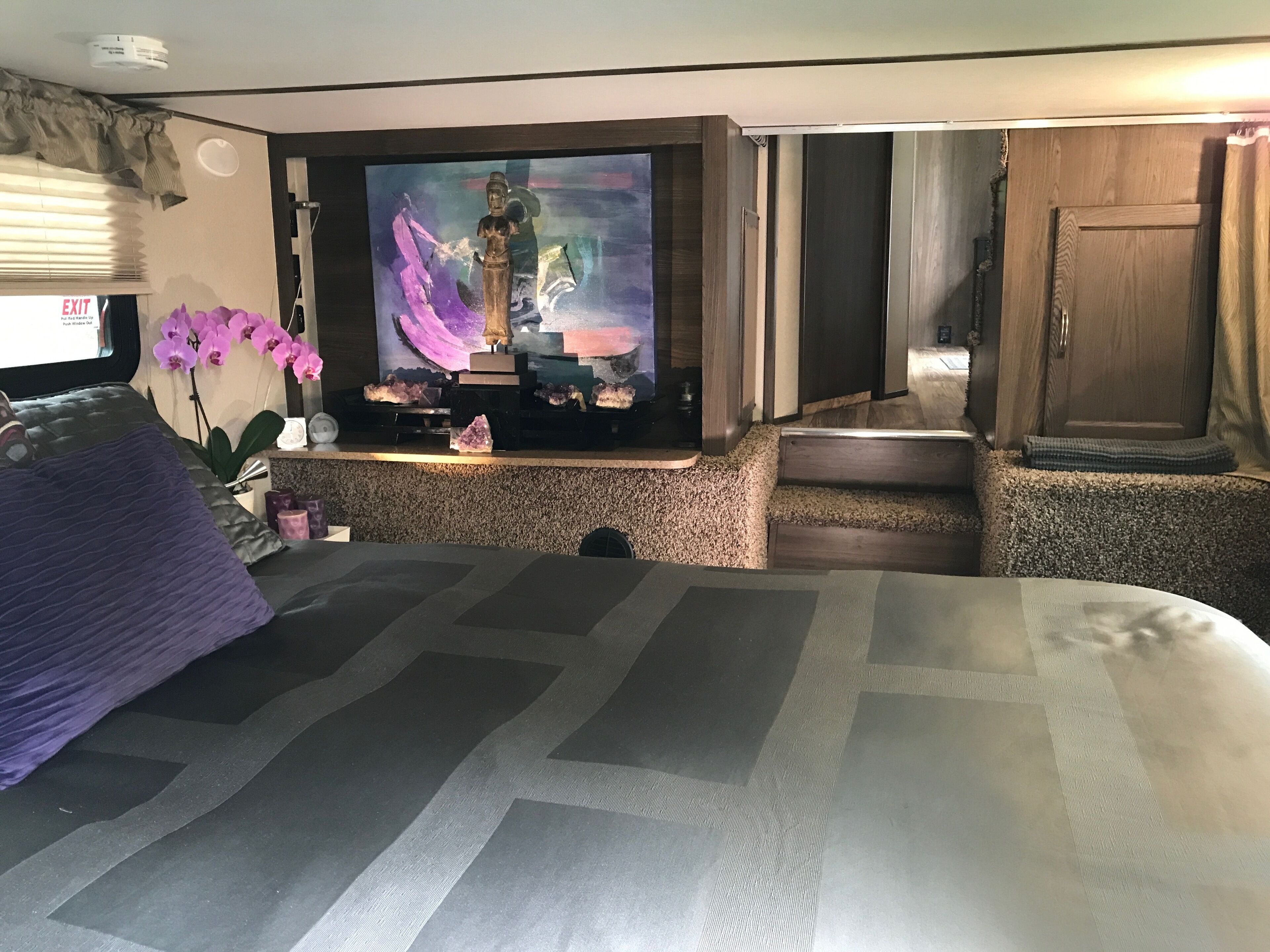 Habitación de hotel con cama, televisión montada en la pared, una mesita con una estatua y una ventana con persianas.