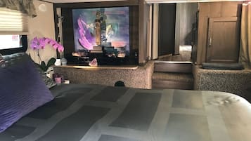 Habitación de hotel con cama, televisión montada en la pared, una mesita con una estatua y una ventana con persianas.