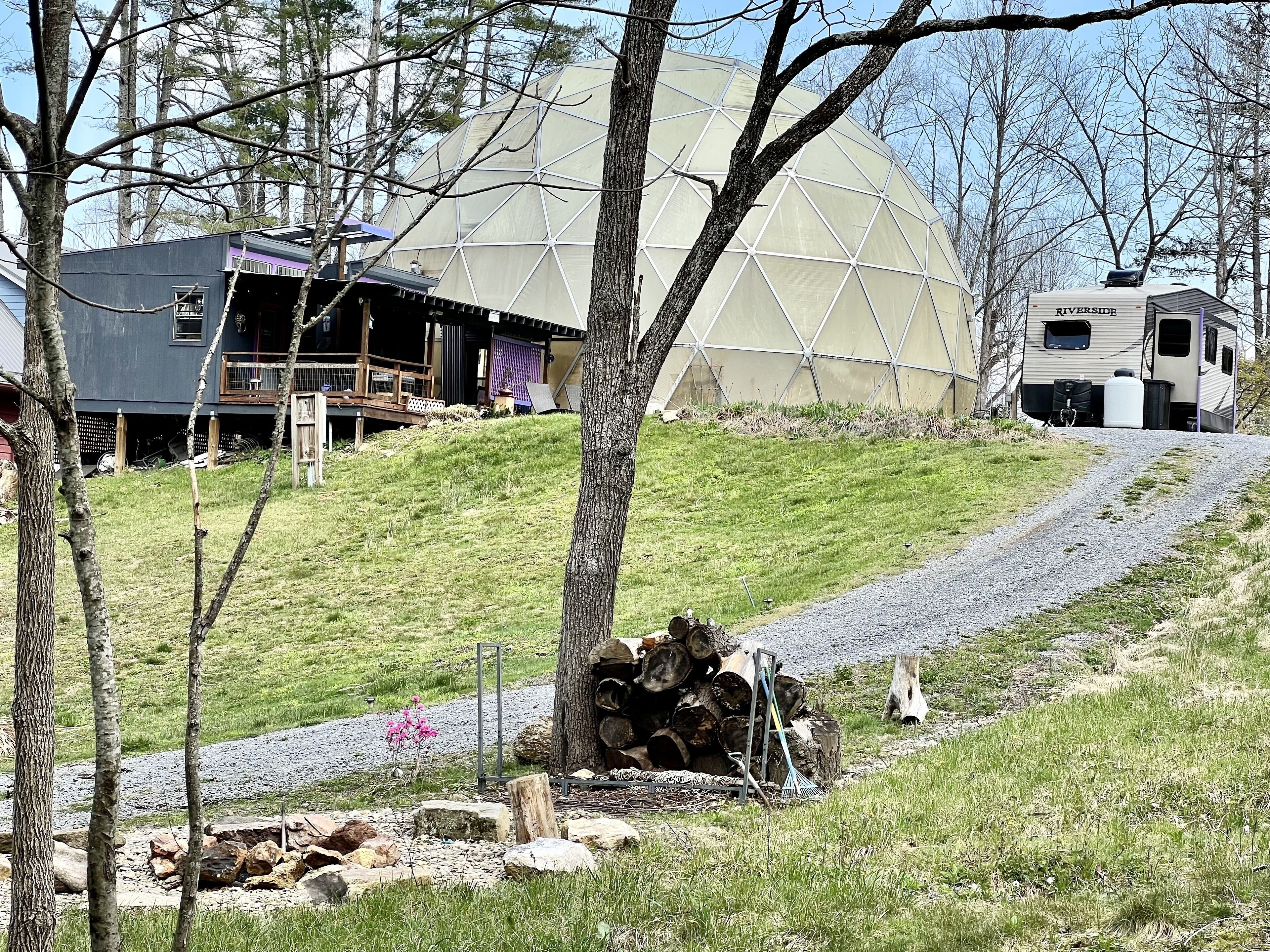 A dome-shaped structure, a covered deck, and a recreational vehicle in a wooded area.