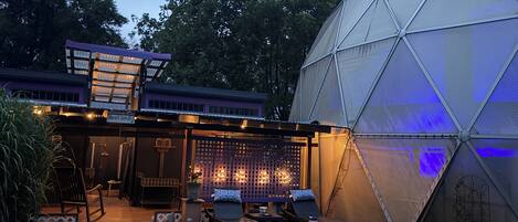Una estructura de invernadero con cúpula, una terraza con asientos exteriores y un área cubierta con luces.
