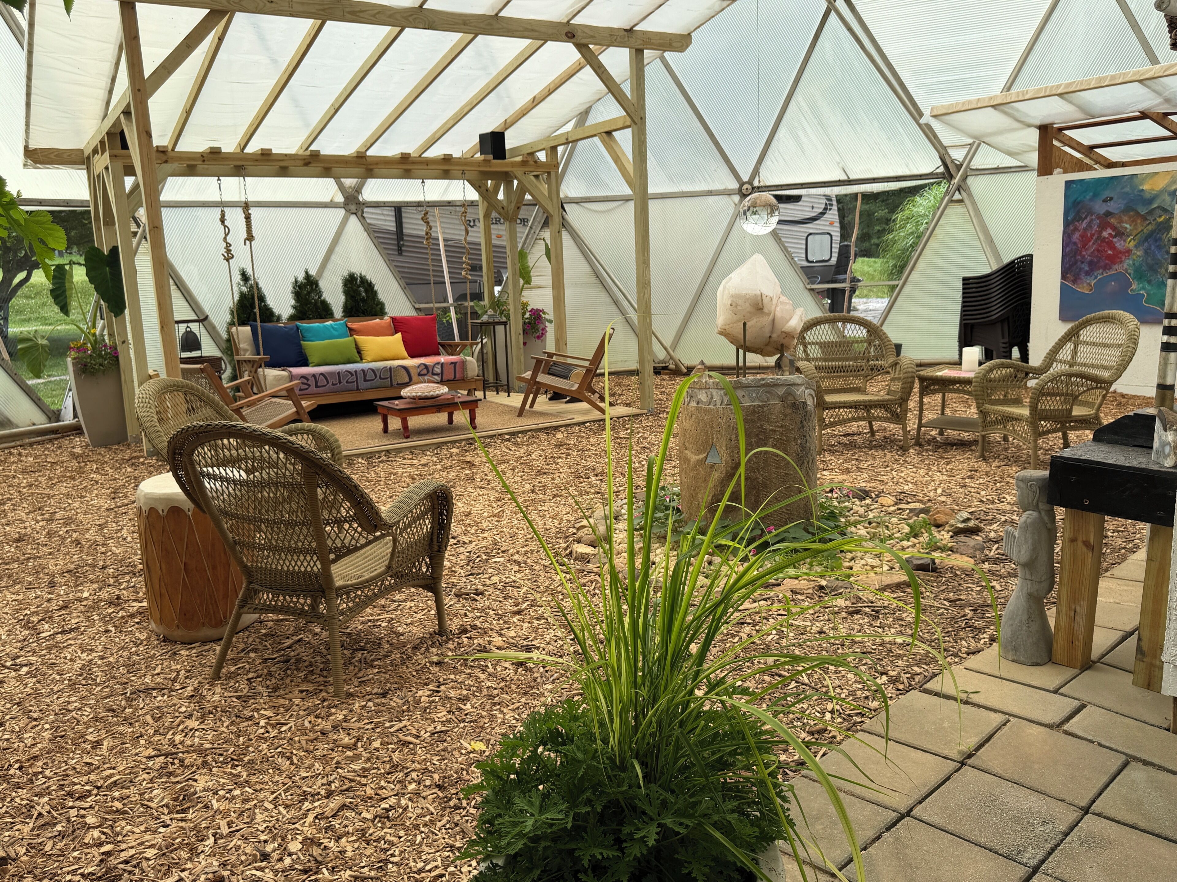 A greenhouse with a wooden pergola, wicker furniture, and a variety of plants.