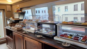 A buffet area with various food items displayed in clear containers, a coffee machine, and a view of the building outside. - Sempione Boutique Hotel (Stresa)
