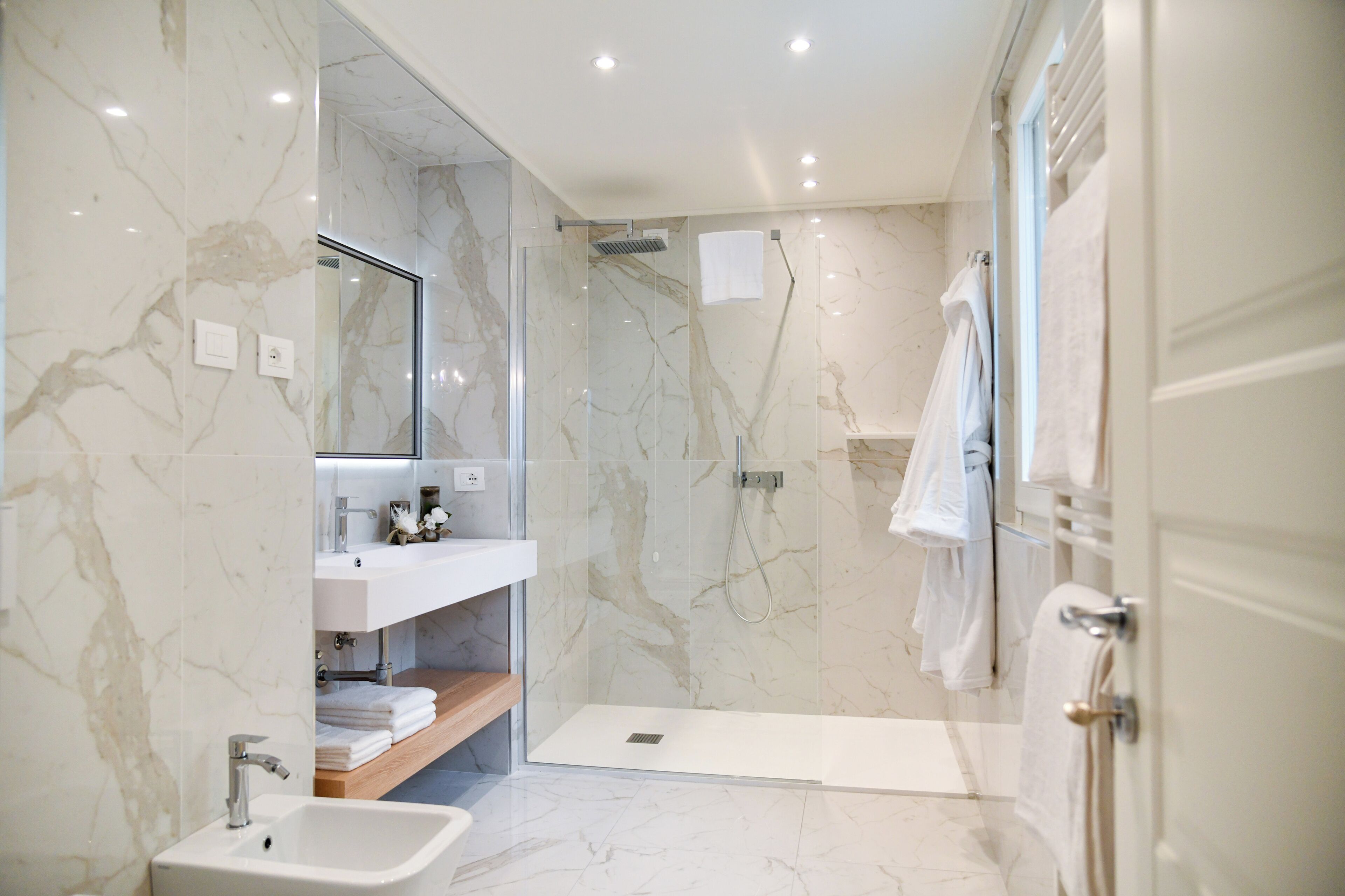 A modern bathroom with a glass-enclosed shower, marble walls, a sink, and a vanity with a mirror.