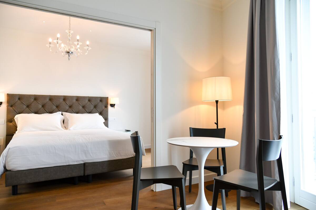 A bedroom with a bed, a chandelier, a round table, and two chairs.