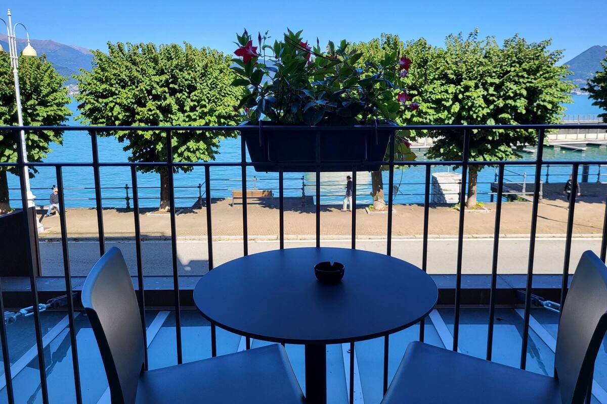 A balcony with a table and chairs, overlooking a waterfront with trees and a distant mountain.