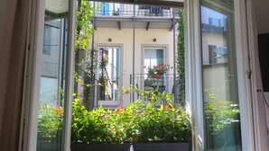 A room with a window overlooking a balcony with plants and a building in the background. - Sempione Boutique Hotel (Stresa)