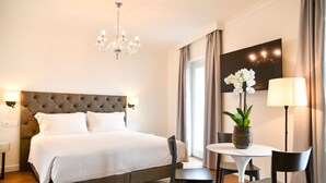 A hotel room with a large bed, a chandelier, a dining table with chairs, and a vase with flowers. - Sempione Boutique Hotel (Stresa)