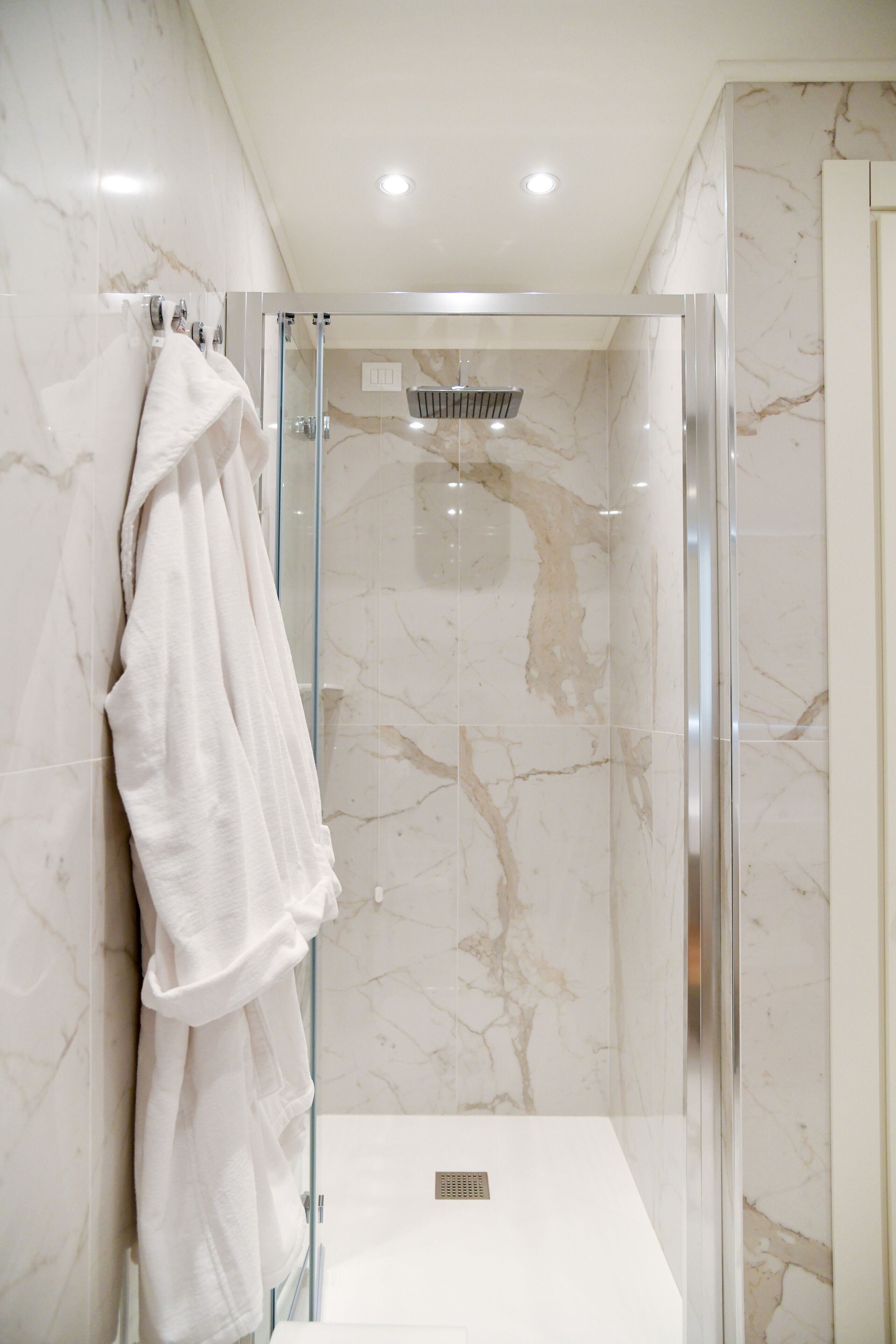 A modern bathroom with a glass-enclosed shower, marble walls, and a white towel hanging on the wall.