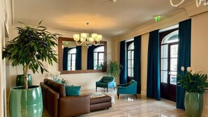 A spacious lobby with a brown leather sofa, teal armchairs, and large green potted plants. - Sempione Boutique Hotel (Stresa)
