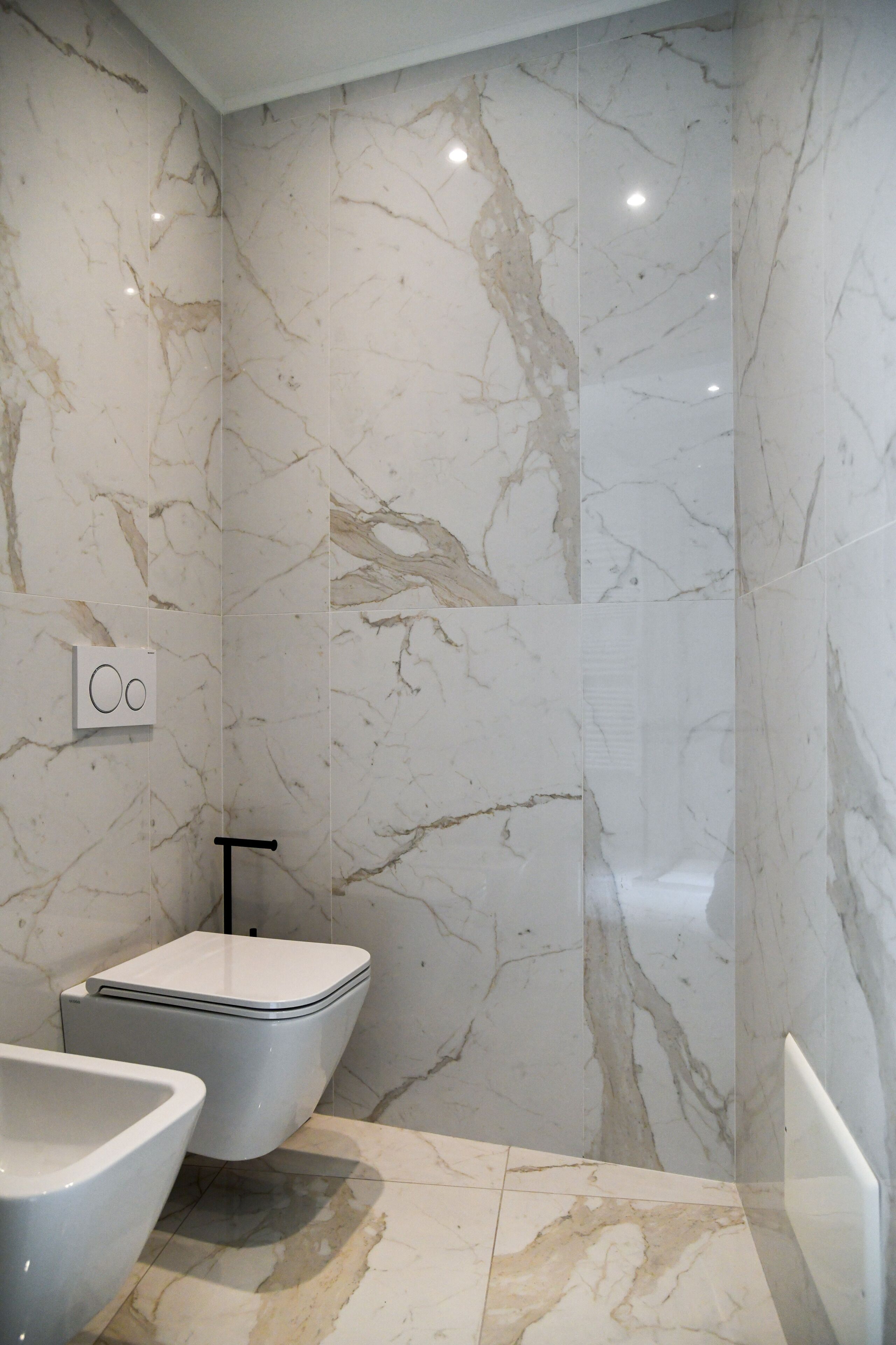 A modern bathroom with marble walls, a toilet, and a bidet.