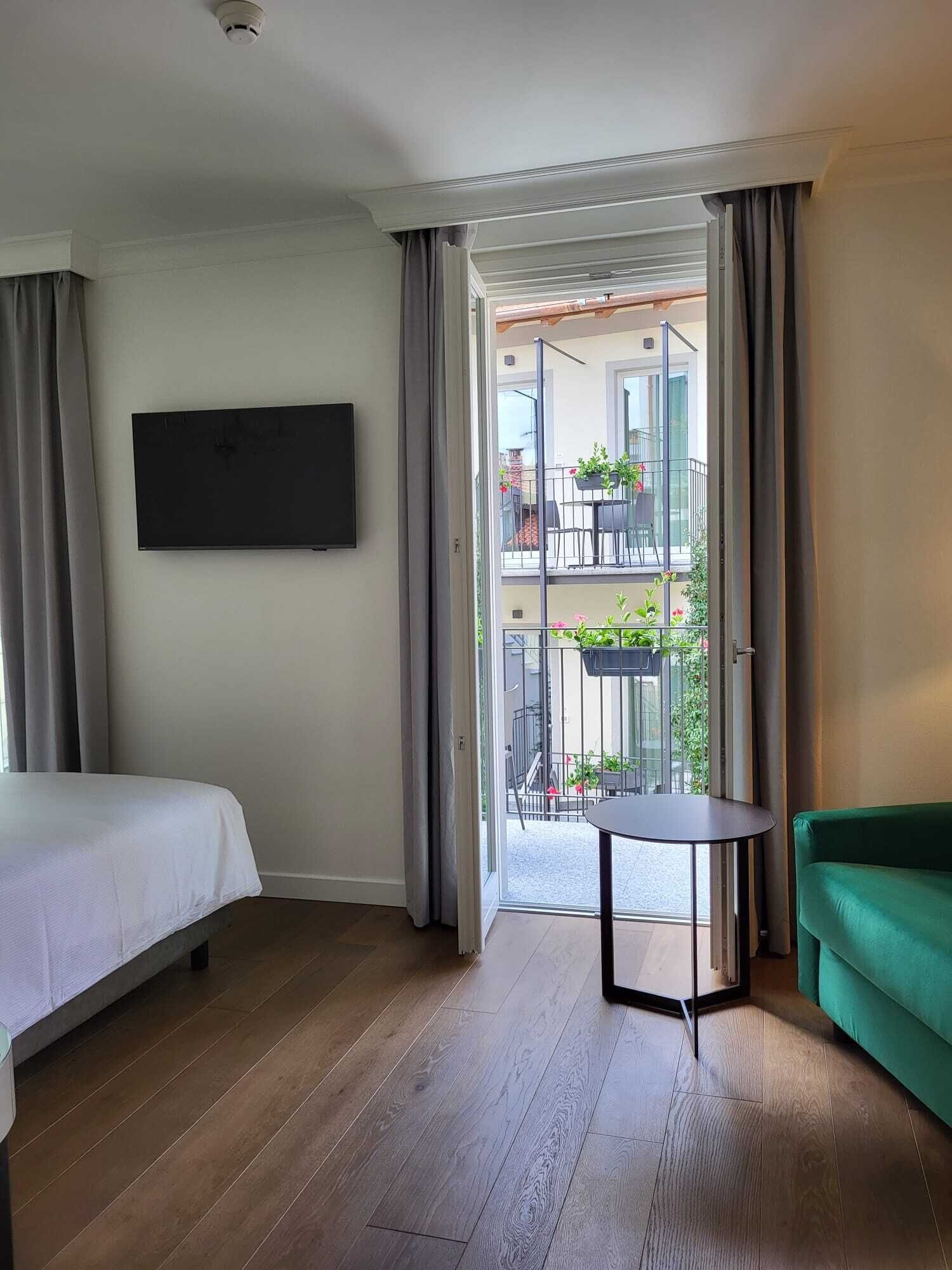 Une chambre d’hôtel avec un lit, une petite table, un canapé vert et un balcon agrémenté de plantes et d’une table.