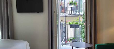 A hotel room with a bed, a small table, a green sofa, and a balcony with plants and a table.