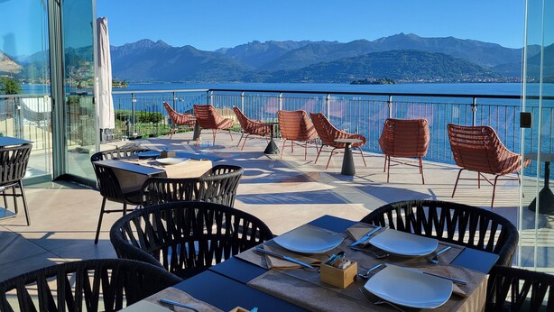 A terrace with tables and chairs, overlooking a lake with mountains in the background. - Sempione Boutique Hotel (Stresa)
