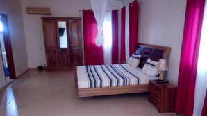 A bedroom with a bed, wooden wardrobe, and a bedside table. - DIOUF HOUSE (Saly)