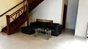 A living room with a black leather sofa, a glass coffee table, and a wooden staircase. - DIOUF HOUSE (Saly)