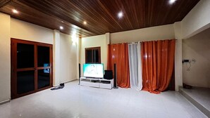 A spacious living area with a wooden ceiling, a sliding glass door, a flat-screen TV, and a window with curtains. - DIOUF HOUSE (Saly)