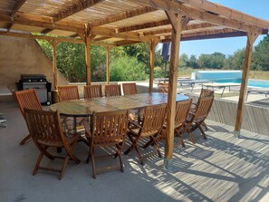 Un espacio de comedor al aire libre con una pérgola de madera, una mesa redonda y sillas.