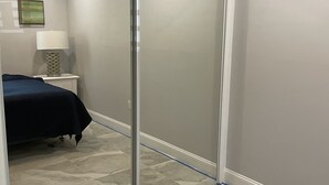 Een slaapkamer met een schuifdeur, een bed met donkerblauwe dekbedovertrek, een nachtkastje met een lamp en een aan de muur hangend schilderij.