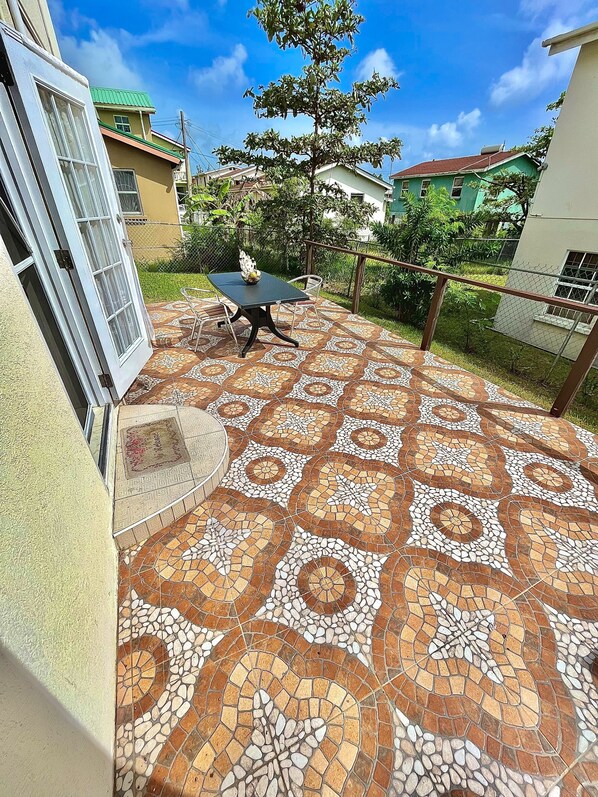 Une terrasse avec un sol carrelé en mosaïque, une table avec des chaises et une petite table ronde sur laquelle est posé un bol.