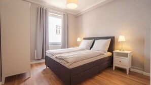 Un dormitorio con cama, mesitas de noche, un armario y una ventana con cortinas.