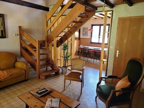 A cozy living room with a wooden staircase, a dining area, and a green armchair. - Family beach house (Ploubazlanec)