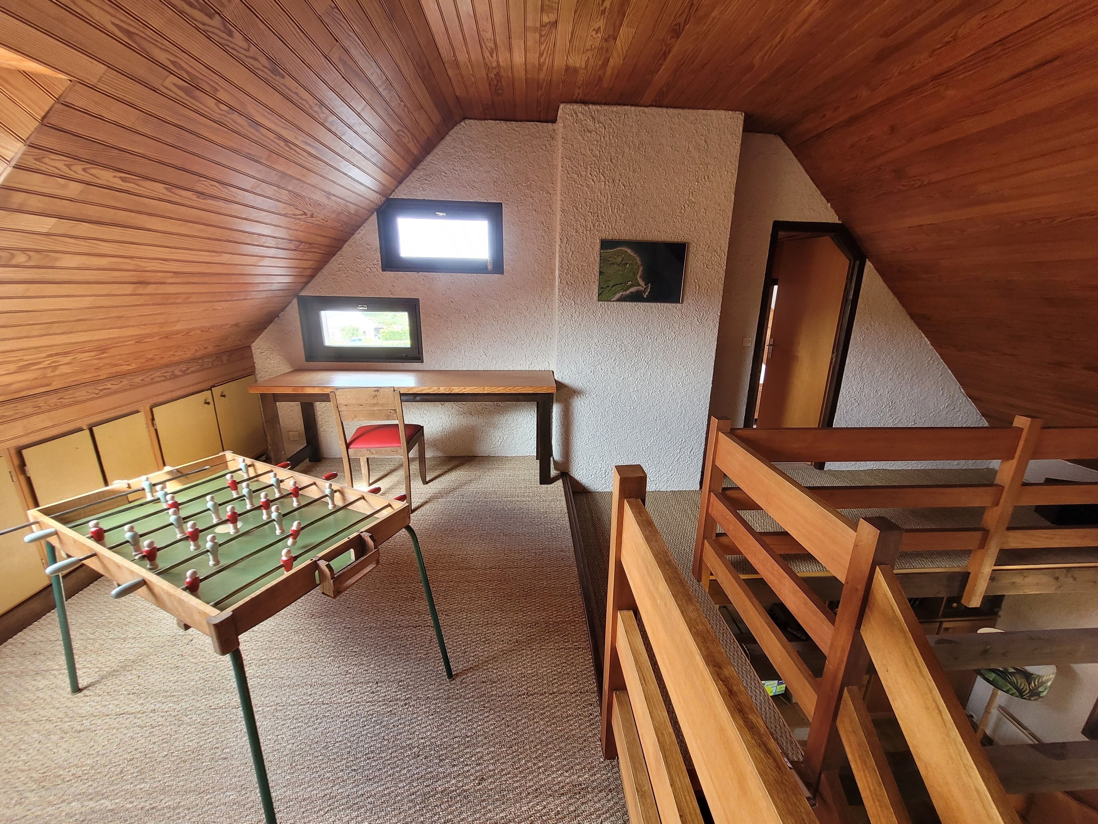 Una habitación cálida en el ático con una mesa de fútbol, un televisor y un escritorio pequeño.