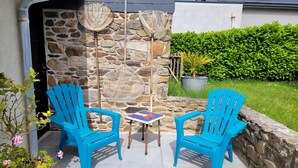Een terras met twee blauwe stoelen en een kleine tafel, een stenen muur en een haag op de achtergrond.