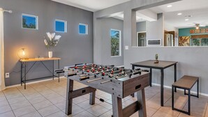 A modern living room with a foosball table, a small table with a plant, and a foosball table on a stand. - Az morning glory 4bedroom home (Buckeye)