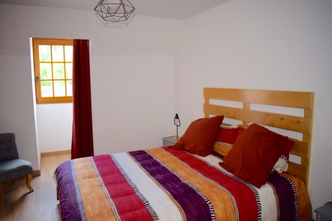 Camera da letto con un letto in legno, biancheria a righe, una sedia, un comodino e una finestra con tende.