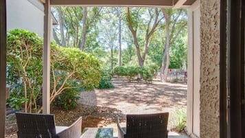 Un porche cubierto con muebles de mimbre y vistas a un jardín ajardinado con árboles y arbustos.