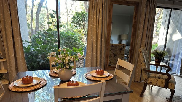 Een eethoek met een glazen tafel, witte stoelen, een vaas met bloemen en een pompoen op een bord.