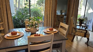 Un comedor con una mesa de vidrio, sillas blancas, un jarrón con flores y una calabaza en un plato.