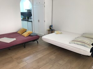 A small, compact room with two beds, a kitchenette, and a white wardrobe.