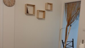 Ein Zimmer mit Holzboden, einer Uhr an der Wand und drei kleinen Holzregalen.