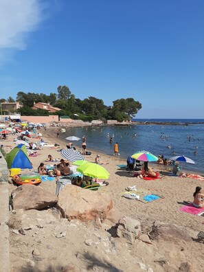 A beach with people sunbathing, swimming, and playing. There are umbrellas, towels, and beach chairs.