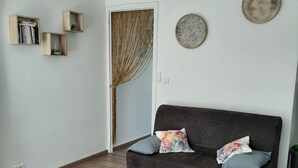 Ein Wohnzimmer mit einem dunkelgrauen Sofa, zwei Kissen, einem gewebten Vorhang und zwei Wandtafeln.
