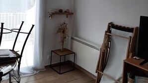 Ein Zimmer mit Klimaanlage, einem gerahmten Bild an der Wand, einem kleinen Holztisch mit einer Pflanze und einem Stuhl mit Kunststoffbezug.