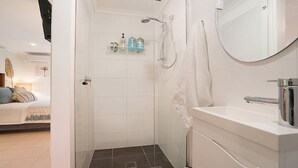 A modern bathroom with a shower, a white sink, and a glass door leading to a bedroom. - Beachside Studio, TOP NOTCH (MACMASTERS BEACH)
