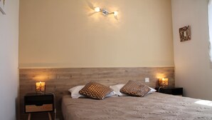 A neatly made bed with a patterned bedspread, two decorative pillows, and a wall-mounted light fixture. - Semi-detached mini-villa in small family residence (San-Gavino-Di-Carbini)