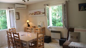 A dining area with a table and chairs, a window with curtains, a radiator, and a sofa with a cushion labeled "HOME". - Semi-detached mini-villa in small family residence (San-Gavino-Di-Carbini)