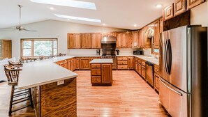 A spacious kitchen with wooden cabinets, a large island, and stainless steel appliances. - Cozy Cabin on the River  (Topton)