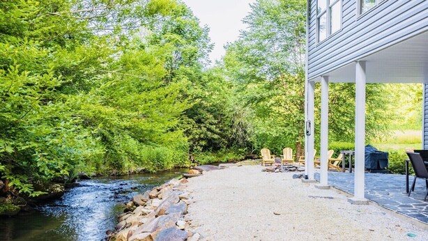 A covered patio area with a gravel path, wooden chairs, and a grill. - Cozy Cabin on the River  (Topton)